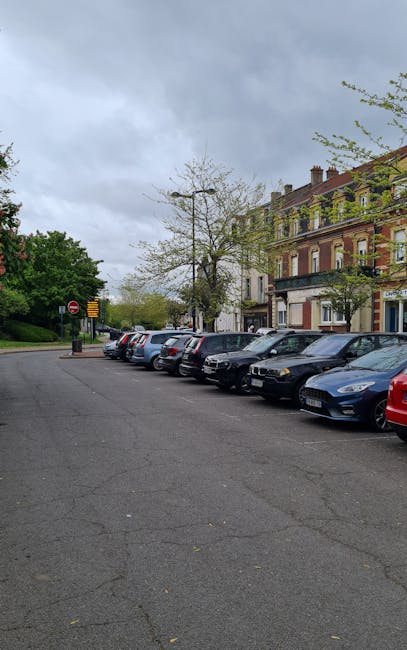 A residential street in Chessington lined with red brick Victorian-style terraced houses featuring white window frames and bay windows. The street is filled with parked cars of various models and colo